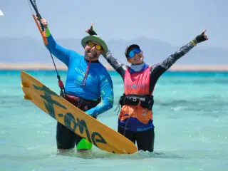 Dwoje uśmiechniętych kitesurferów na płytkiej wodzie, radośnie świętujących udane wyjazdy kitesurfingowe z KiteAway.