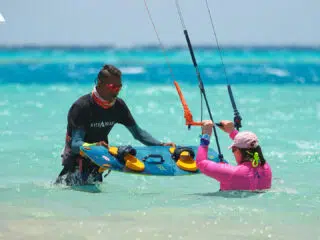 Mężczyzna i kobieta w płytkiej, lazurowej wodzie szykują sprzęt na wakacje z kitesurfingiem z KiteAway - idealny wyjazd z latawcem.