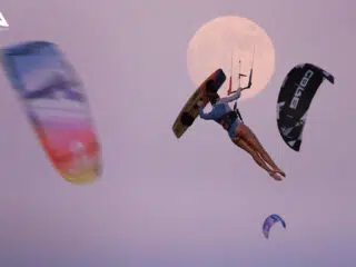 Kitesurfer unosi się wysoko przy pełni księżyca na wyjeździe KiteAway, kolorowe latawce i fioletowe niebo - wyjazdy kitesurfingowe.