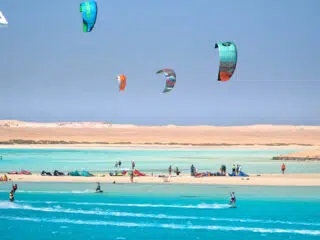 Kitesurferzy na turkusowej wodzie, kolorowe latawce, kite camp KiteAway na plaży. Idealne miejsce na wyjazdy kitesurfingowe.