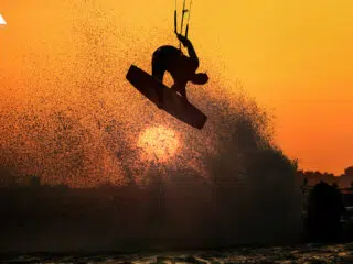 Sylwetka kitesurfera w skoku na tle miasta i zachodu słońca - idealny klimat na wyjazdy kitesurfingowe z KiteAway.