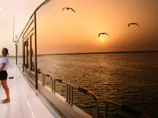 Kobieta na pokładzie łodzi podczas kite tripu KiteAway, patrzy na morze o zachodzie słońca - idealne wakacje z kitesurfingiem.