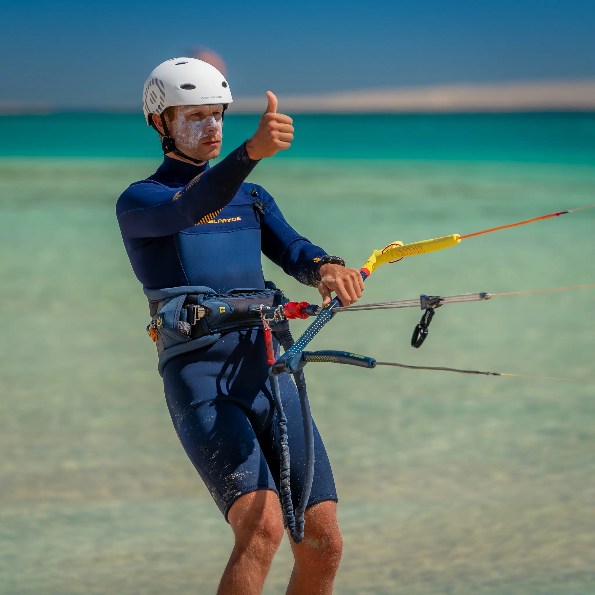 Uśmiechnięty uczestnik wyjazdu kitesurfingowego KiteAway w piance i kasku, na tle turkusowej wody podczas kite safari.
