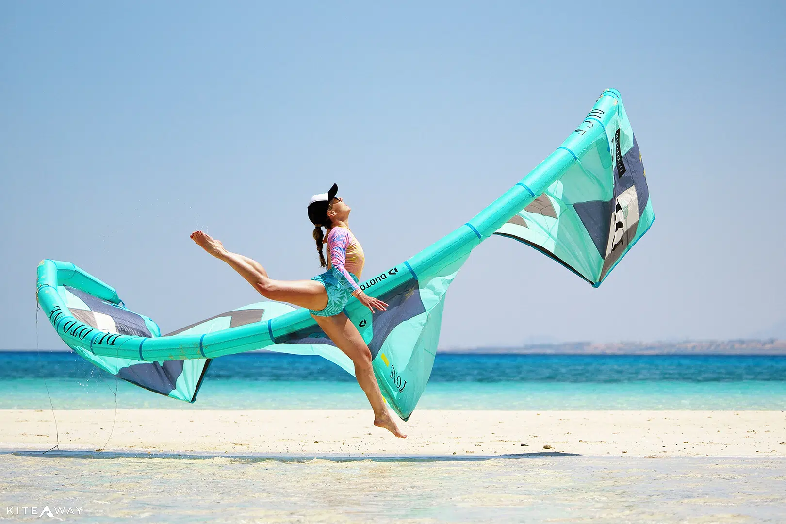 Kitesurferka skacze z latawcem na plaży z turkusową wodą - radość z wyjazdu kitesurfingowego KiteAway, idealne wakacje z kitesurfingiem.