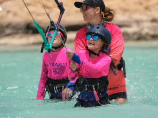 Dwoje dzieci w różowych koszulkach i instruktor uśmiechnięci podczas kursu kitesurfingu KiteAway na wakacjach z kitesurfingiem.