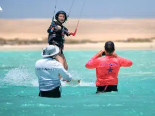 Kurs kitesurfingu KiteAway - kobieta trenuje na turkusowej wodzie, instruktorzy asystują; wyjazdy kitesurfingowe, kite camp.