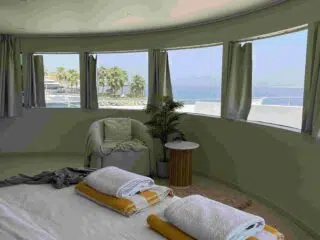 Jasny pokój z widokiem na palmy i morze, idealny na wyjazdy kitesurfingowe KiteAway; wygodne łóżko, ręczniki i fotel.