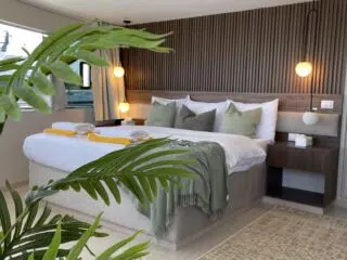 Nowoczesna sypialnia z motywami kite tripu KiteAway, zielona narzuta, podwójne łóżko i duże okno - klimat wyjazdów kitesurfingowych.