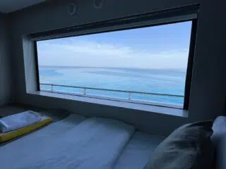 Łóżko z białą pościelą przy oknie z widokiem na morze - idealny relaks po szkoleniu kite na wyjazdach kitesurfingowych KiteAway.