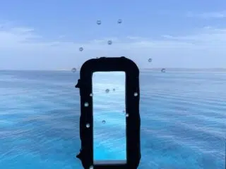 Widok przez okno z kroplami wody na lazurowe morze podczas wyjazdu kitesurfingowego KiteAway - Twoje idealne wakacje z kitesurfingiem.