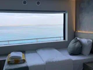 Przytulne łóżko z białą pościelą przy oknie z widokiem na ocean, idealne na wyjazdy kitesurfingowe z KiteAway.