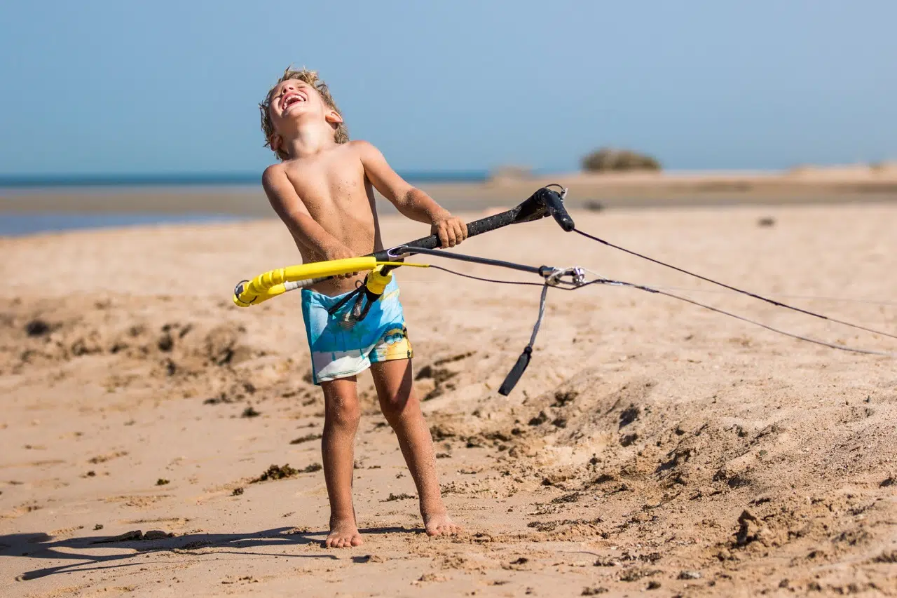 Chłopiec w niebieskich kąpielówkach bawi się na plaży El Gouny, trzymając bar kite. Wakacje z kitesurfingiem KiteAway, Egipt.