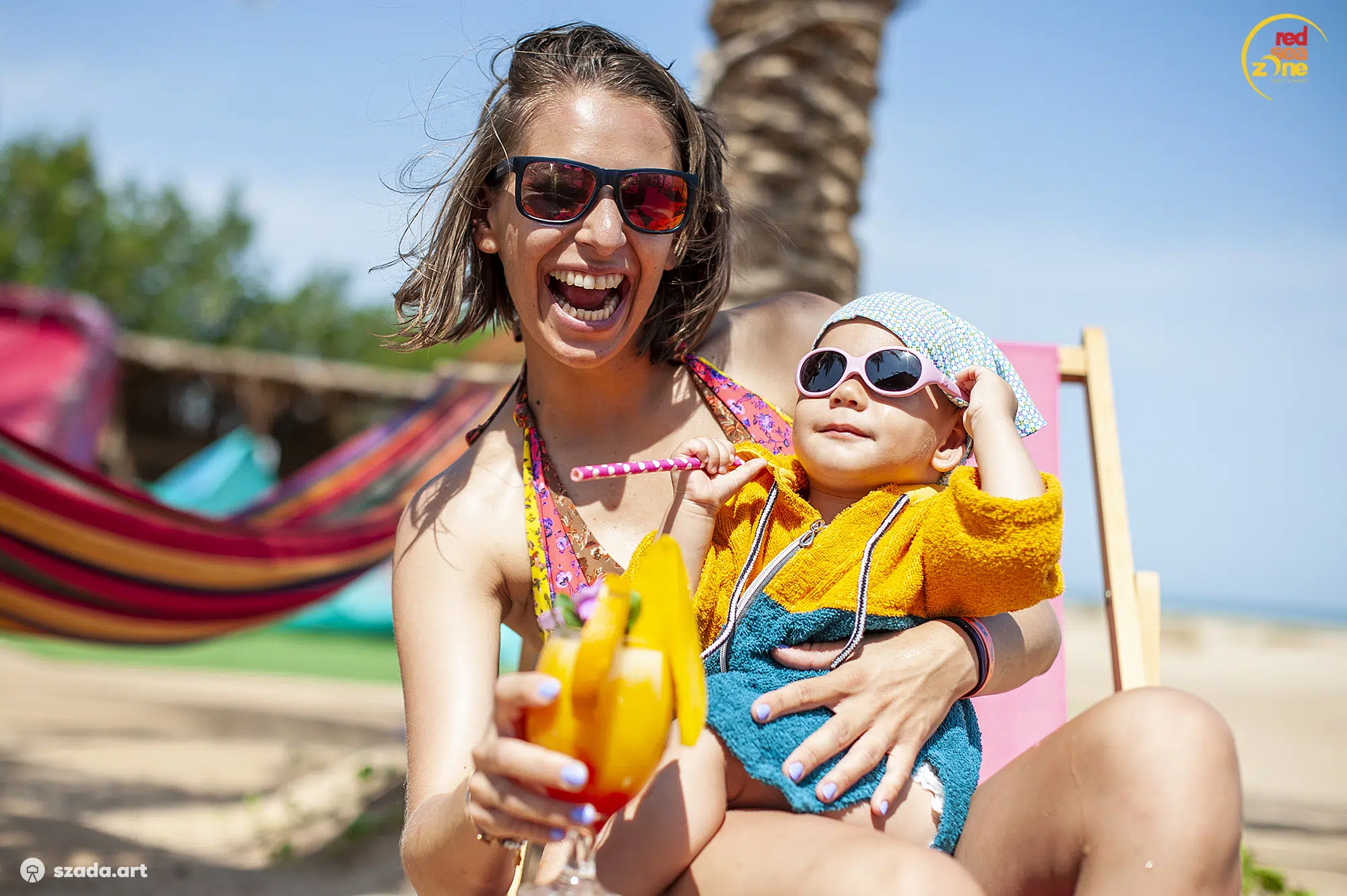 Uśmiechnięta kobieta z dzieckiem relaksuje się na plaży El Gouna w otoczeniu palm - wakacje z kitesurfingiem z KiteAway.