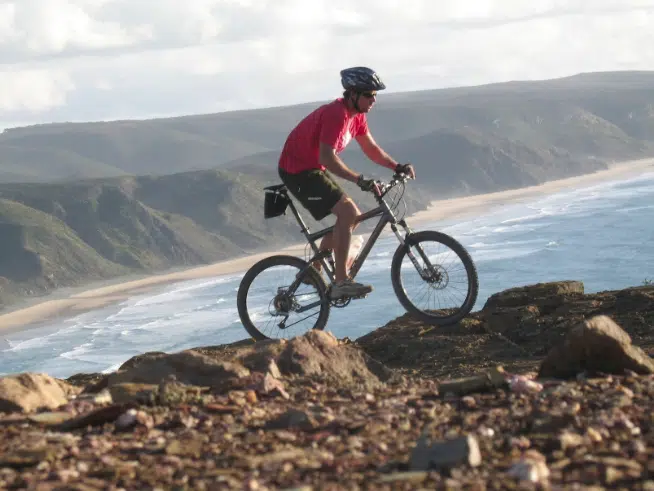 Osoba na rowerze górskim z widokiem na wybrzeże Portugalii - idealny spot na wakacje z kitesurfingiem z KiteAway.