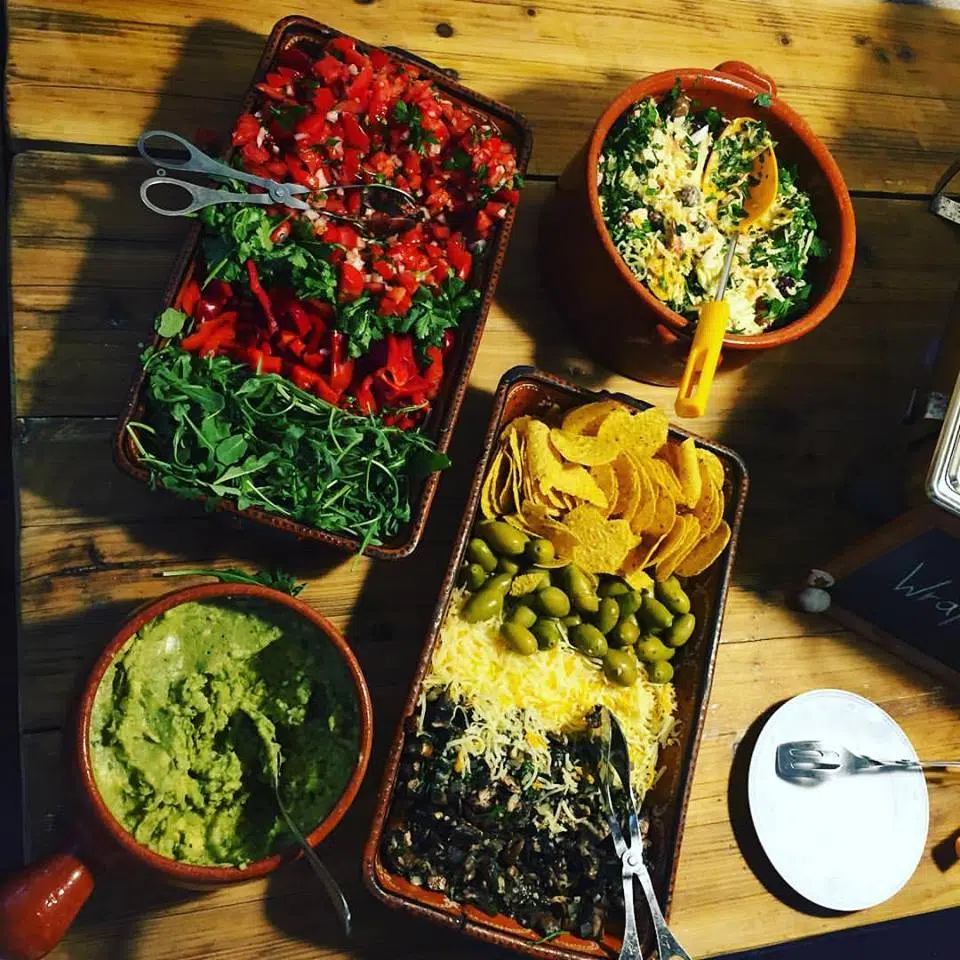 Stół z potrawami: sałatki, nachosy, guacamole - idealny posiłek po dniu na kite campie KiteAway w Portugalii.