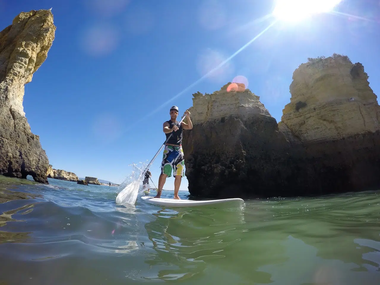 Paddleboarding na zielonej wodzie przy klifach, na tle kitesurfingu w Portugalii - kite camp i wakacje z KiteAway.pl.