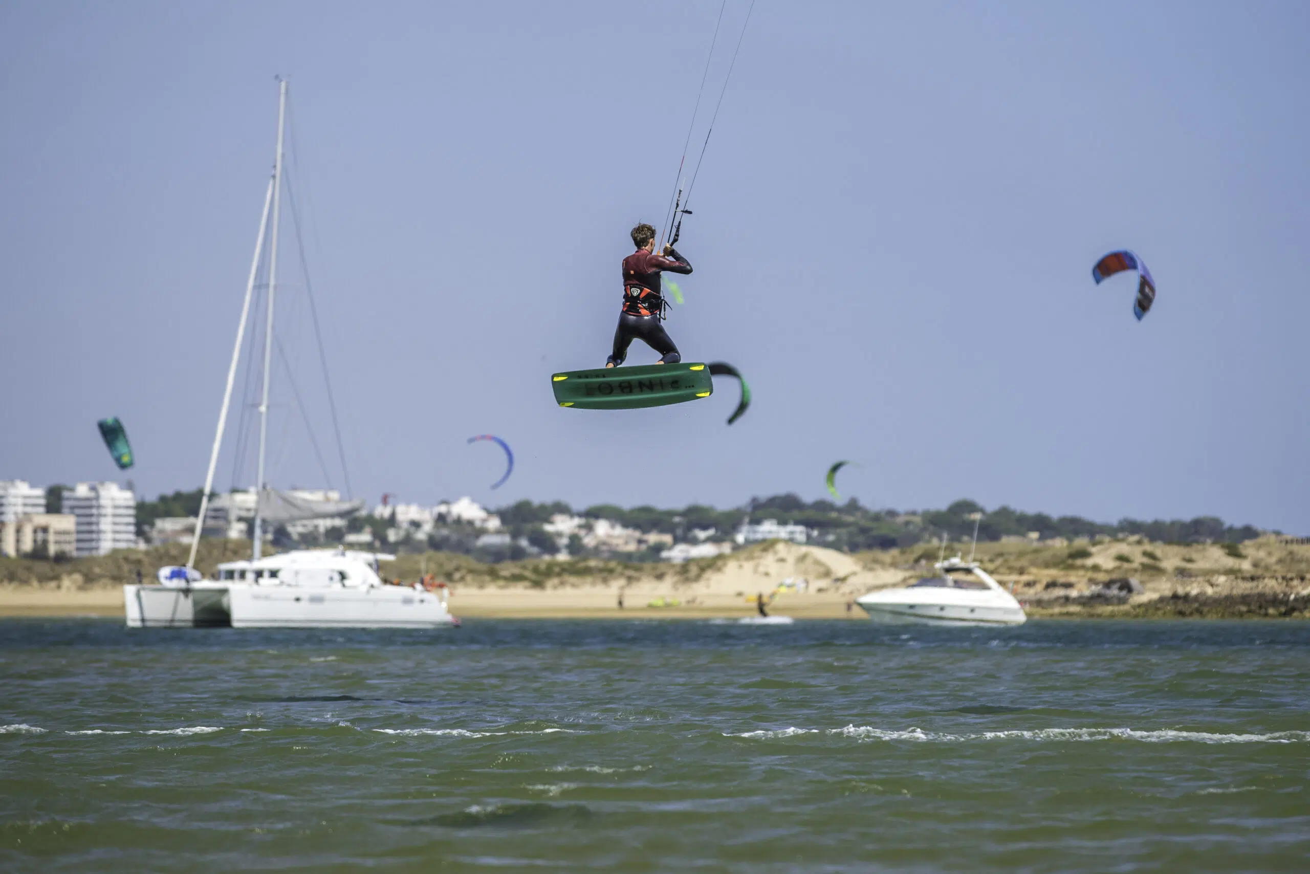 Kitesurfer w powietrzu nad wodą w Portugalii, na tle kite campu KiteAway i innych uczestników wyjazdu kitesurfingowego.