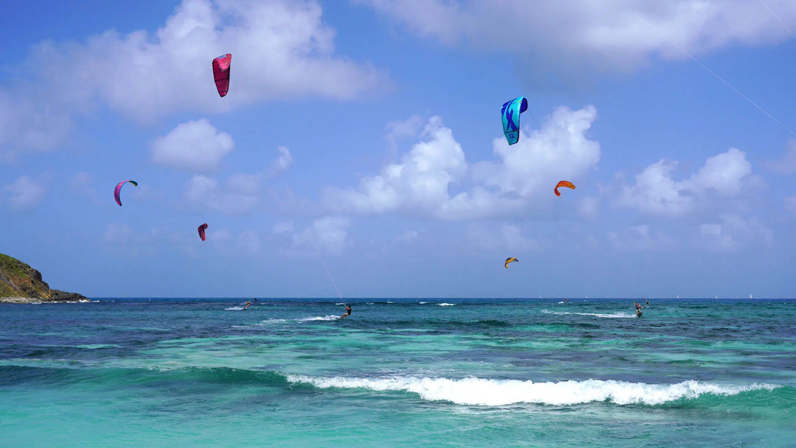 Kitesurferzy na turkusowym oceanie podczas wyjazdu KiteAway; kolorowe latawce i fale, idealne wakacje z kitesurfingiem.
