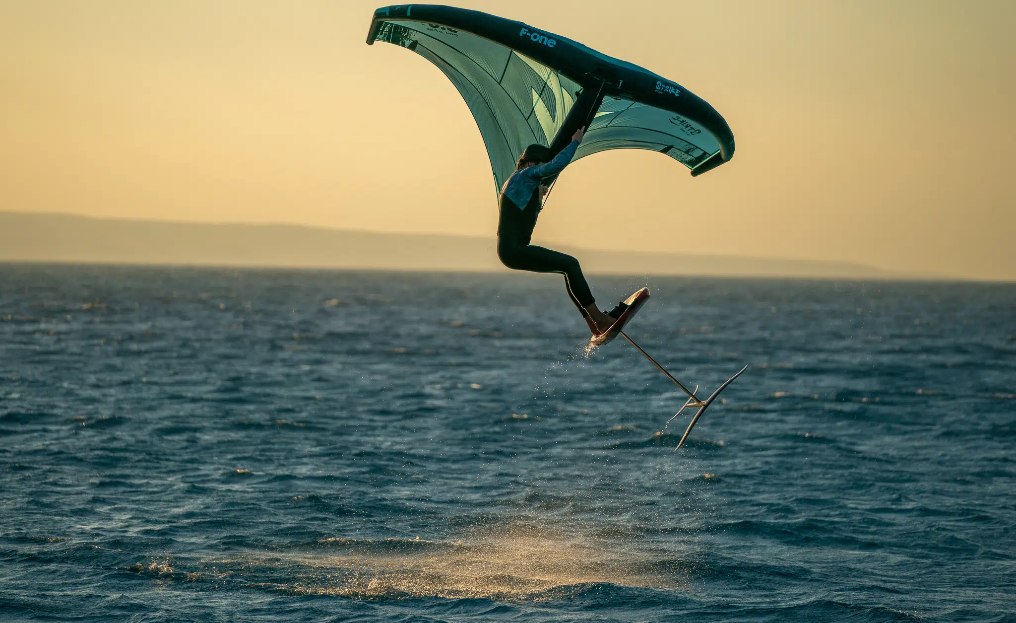 Kitesurfer na hydrofoilu z latawcem unosi się nad wodą o zachodzie słońca - idealny kite trip z KiteAway, wyjazdy kitesurfingowe.