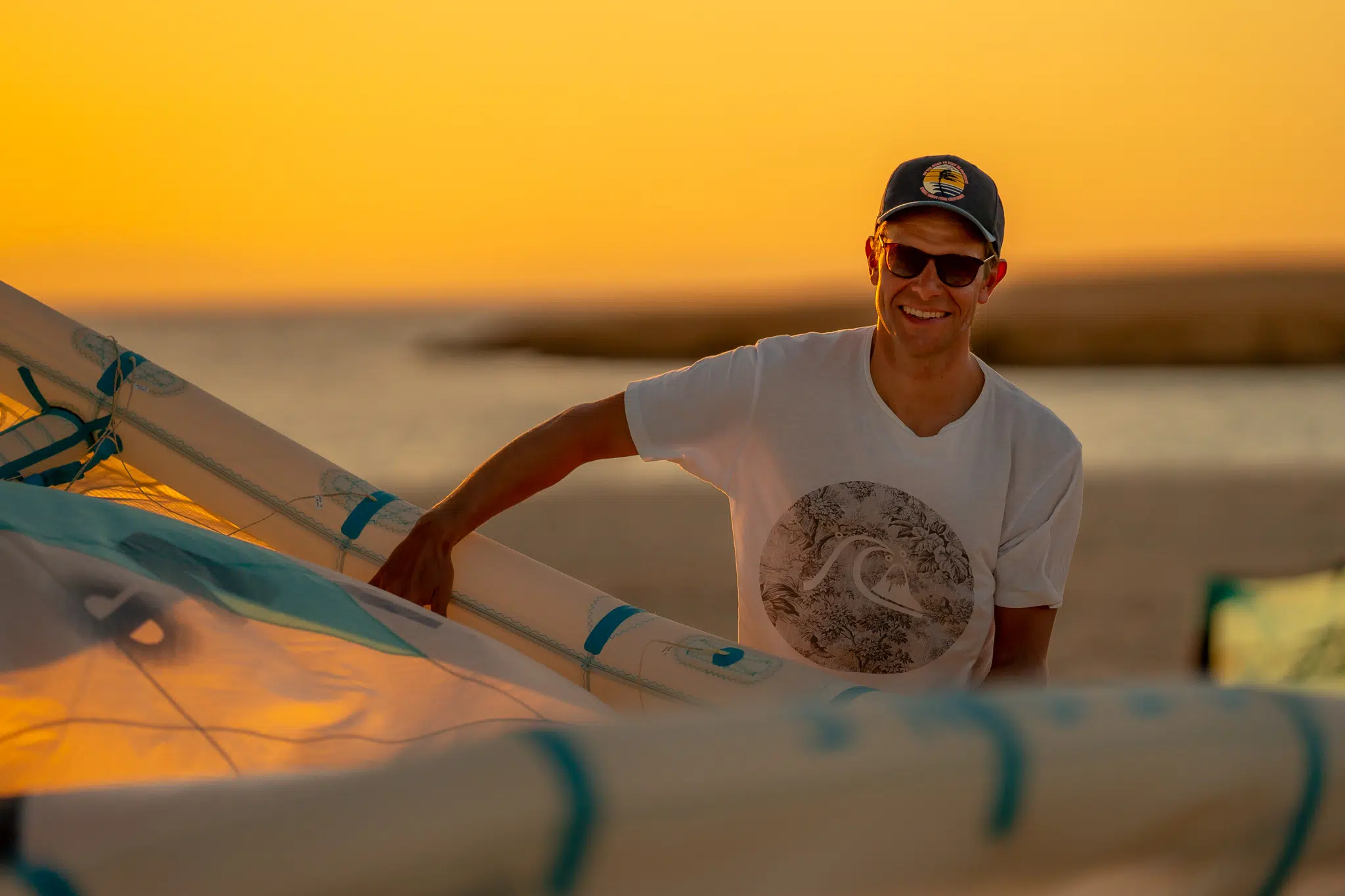 Uśmiechnięty mężczyzna na plaży o zachodzie słońca z deską kite, podczas wyjazdu kitesurfingowego KiteAway.