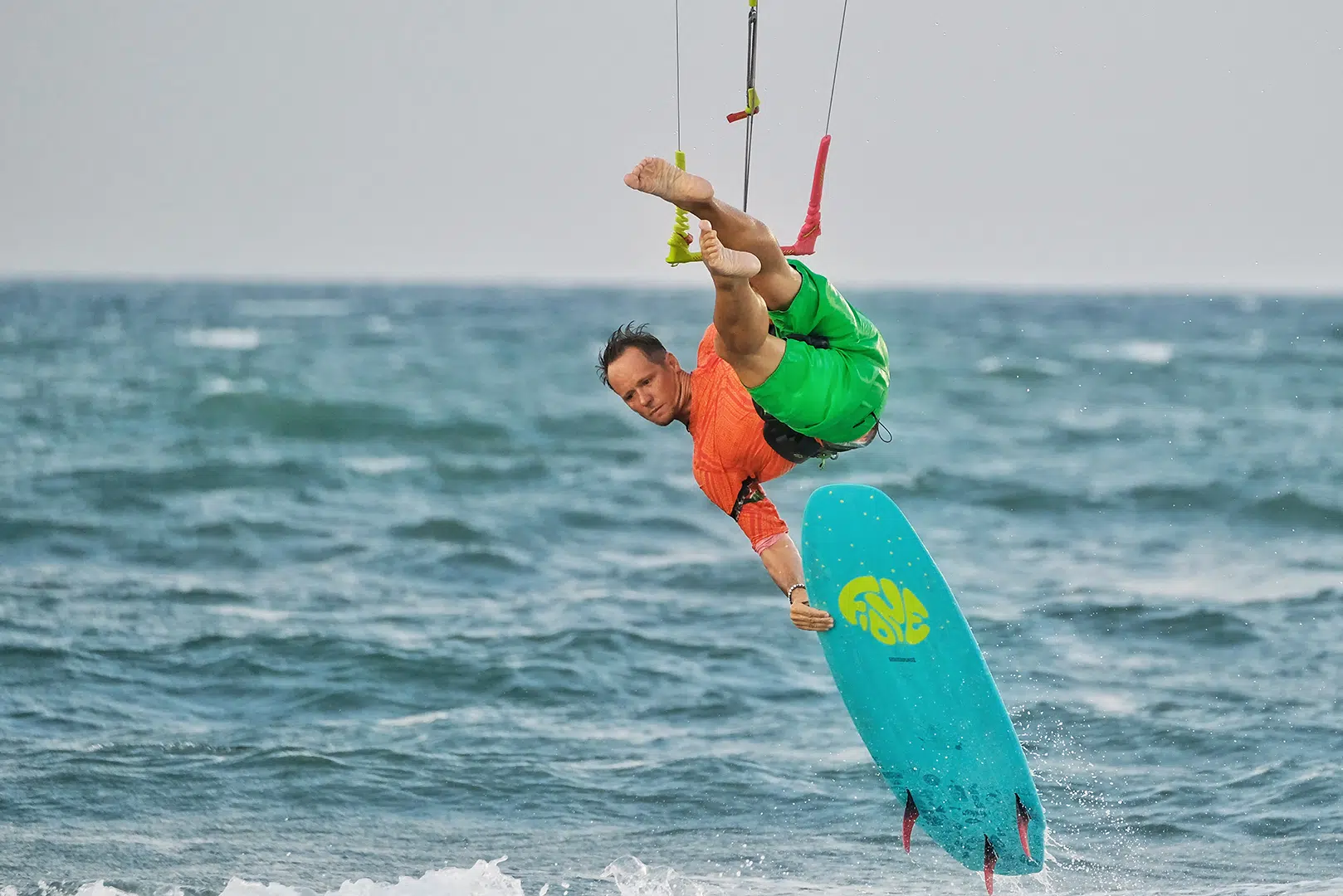 Kitesurfer w pomarańczowej koszulce wykonuje powietrzny trip nad oceanem na Sri Lance podczas wyjazdu kitesurfingowego KiteAway.