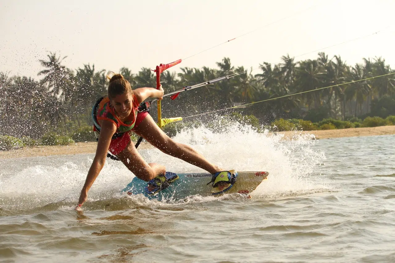 Kobieta w czerwonym stroju kiteboarduje na Sri Lance - kite camp z KiteAway, plaża, palmy i idealne warunki na wyjazdy kitesurfingowe.
