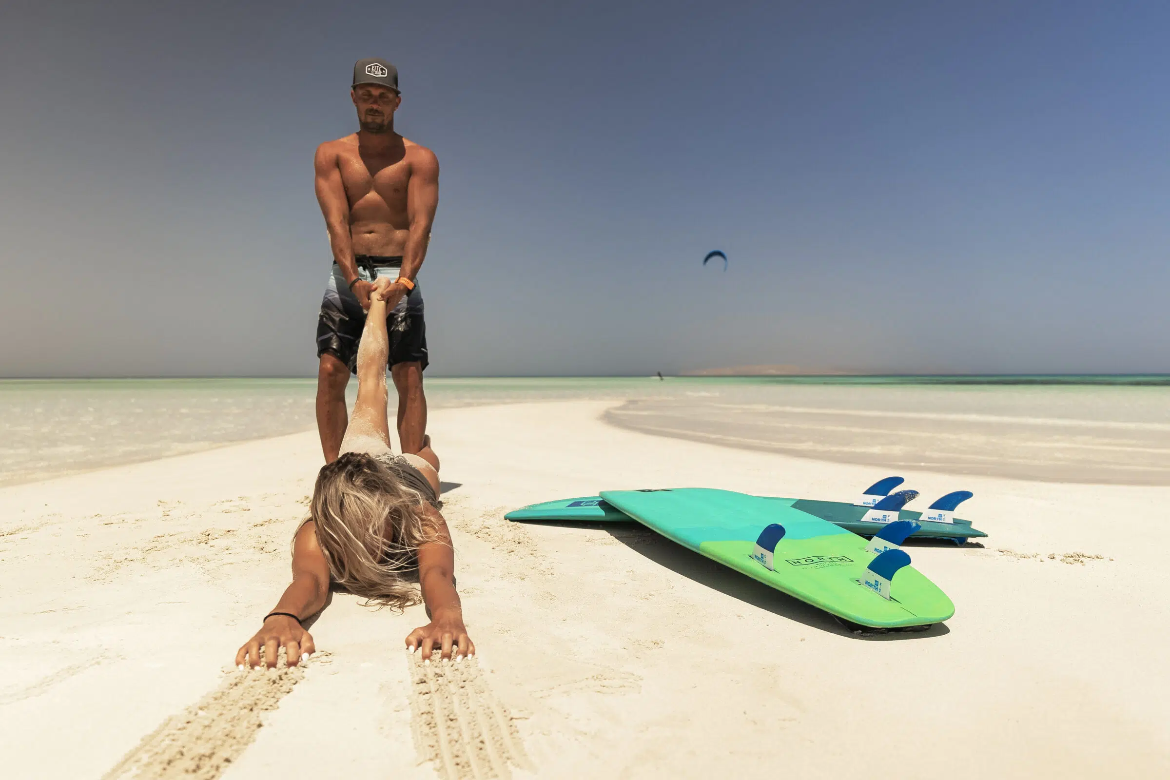 Para na plaży KiteAway - na ciągnie ją za ręce obok desek, w tle kitesurfing i idealny spot na wyjazdy kitesurfingowe.