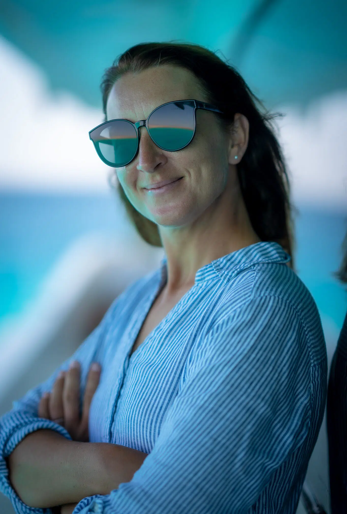 Uśmiechnięta kobieta w okularach i niebieskiej bluzce na tle kite spotu, idealna na wyjazdy kitesurfingowe z KiteAway.