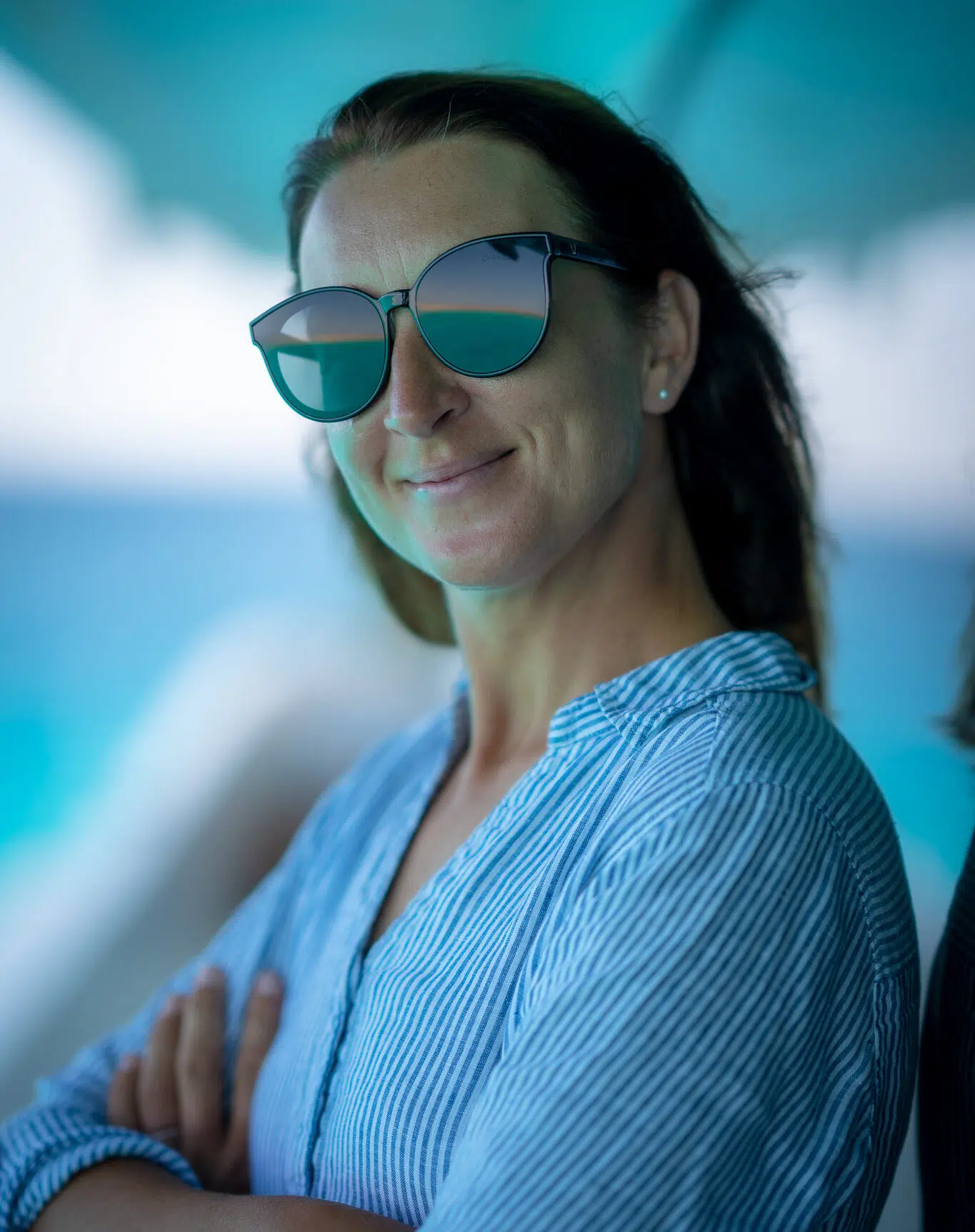 Uśmiechnięta kobieta w okularach przeciwsłonecznych na tle wody - wakacje z kitesurfingiem KiteAway, idealny kite trip.