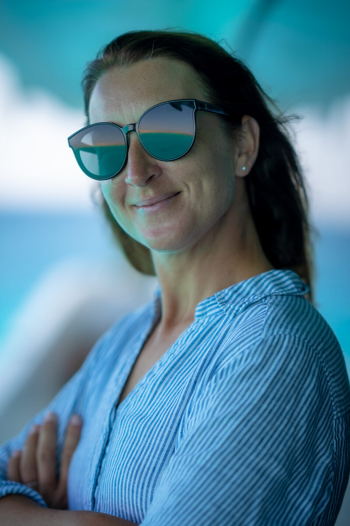 Uśmiechnięta kobieta w okularach przeciwsłonecznych na tle wody - wakacje z kitesurfingiem KiteAway, idealny kite trip.