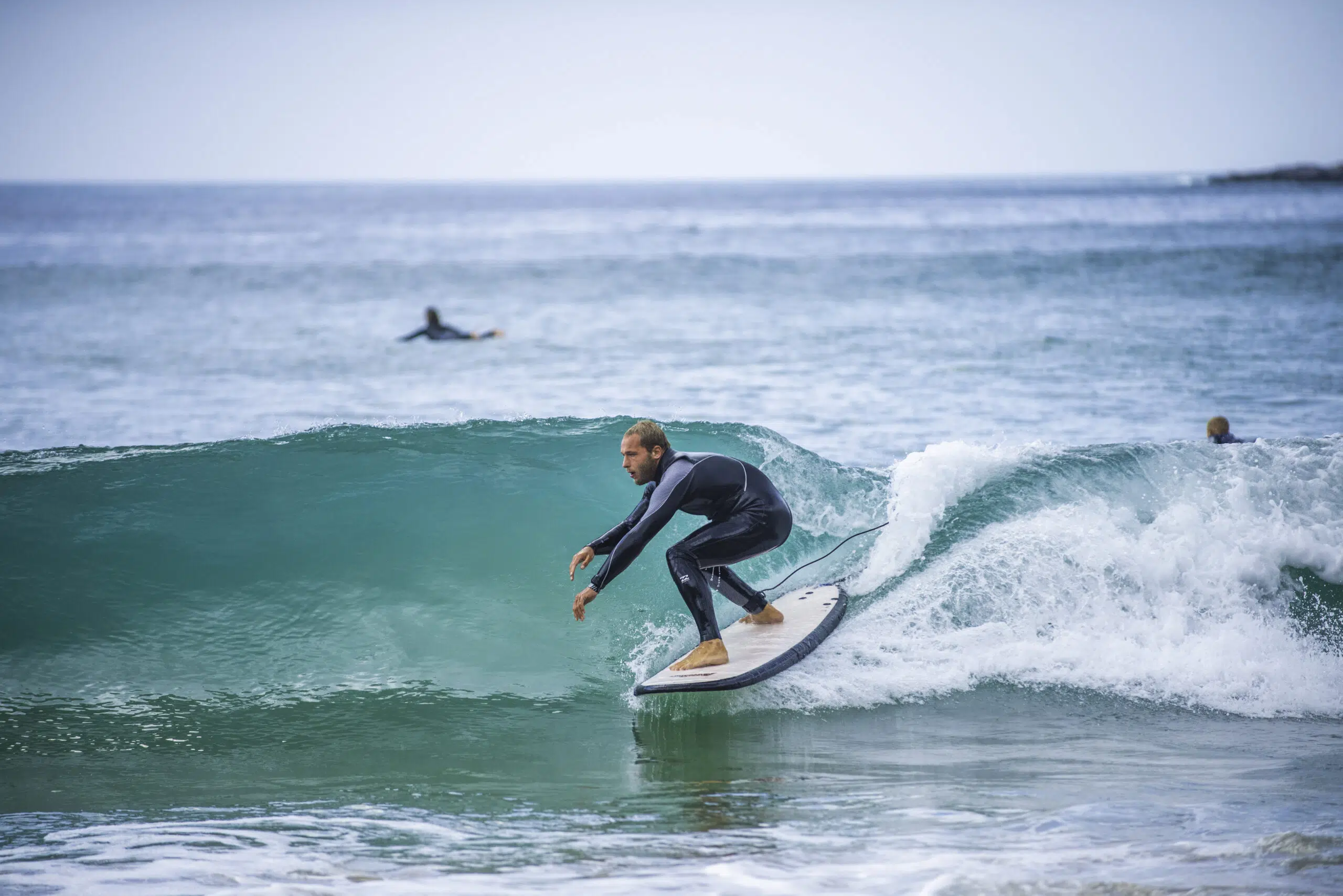 Kitesurfer w czarnym piance na fali blisko brzegu w Portugalii, na tle innych uczestników wyjazdu kitesurfingowego KiteAway.