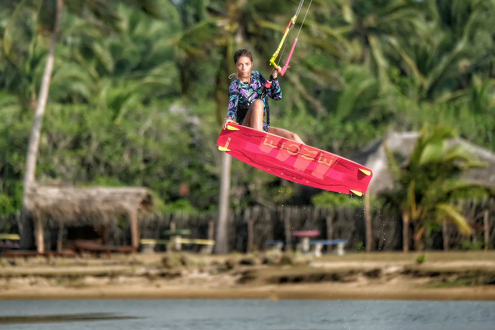 Kitesurferka w kolorowej lycrze skacze z różową deską na wyjeździe KiteAway Sri Lanka; wakacje z kitesurfingiem, kite camp.
