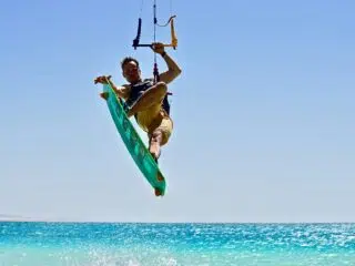 Kitesurfer wykonuje efektowny trick nad turkusową wodą podczas wyjazdu kitesurfingowego KiteAway, pod słonecznym niebem.