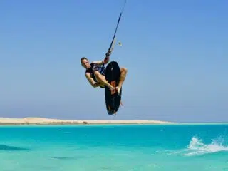 Kitesurfer wykonuje skok nad turkusową wodą na tle plaży - idealne miejsce na wyjazdy kitesurfingowe z KiteAway.
