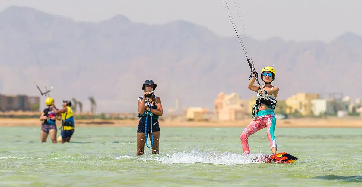 Grupa kobiet podczas wyjazdu kitesurfingowego KiteAway, stoi i pływa na kite spocie w płytkiej wodzie, z górami w tle.