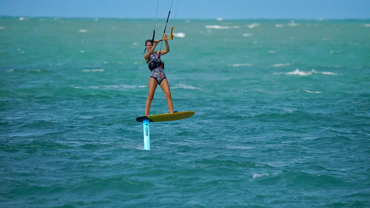 Wyjazd kitesurfingowy z KiteAway: osoba na wodolot płynie po turkusowej wodzie, trzymając bar, przy pięknej pogodzie.