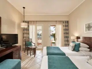 Pokój hotelowy z dwoma łóżkami, biurkiem i TV, z wyjściem na taras przy basenie - idealny na kite trip i wakacje z kitesurfingiem.