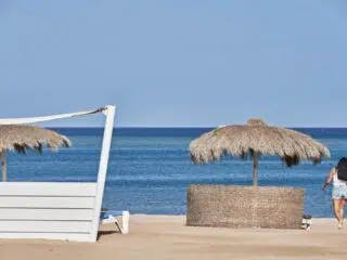 Kobieta idzie po plaży El Gouna ku morzu; w tle kitesurferzy na kite campie KiteAway, idealne miejsce na wyjazdy kitesurfingowe.