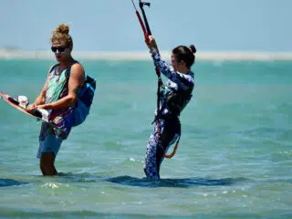 Dwie osoby na płytkiej wodzie ze sprzętem do kitesurfingu podczas wyjazdu KiteAway - idealne wakacje z kitesurfingiem.