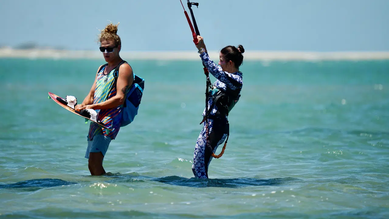 Dwie osoby na płytkiej wodzie ze sprzętem do kitesurfingu podczas wyjazdu KiteAway - idealne wakacje z kitesurfingiem.