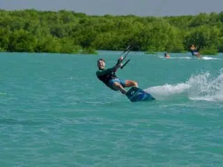 Kiteboarder na turkusowej wodzie podczas wyjazdu kitesurfingowego z KiteAway; w tle drugi rider i zielone drzewa.