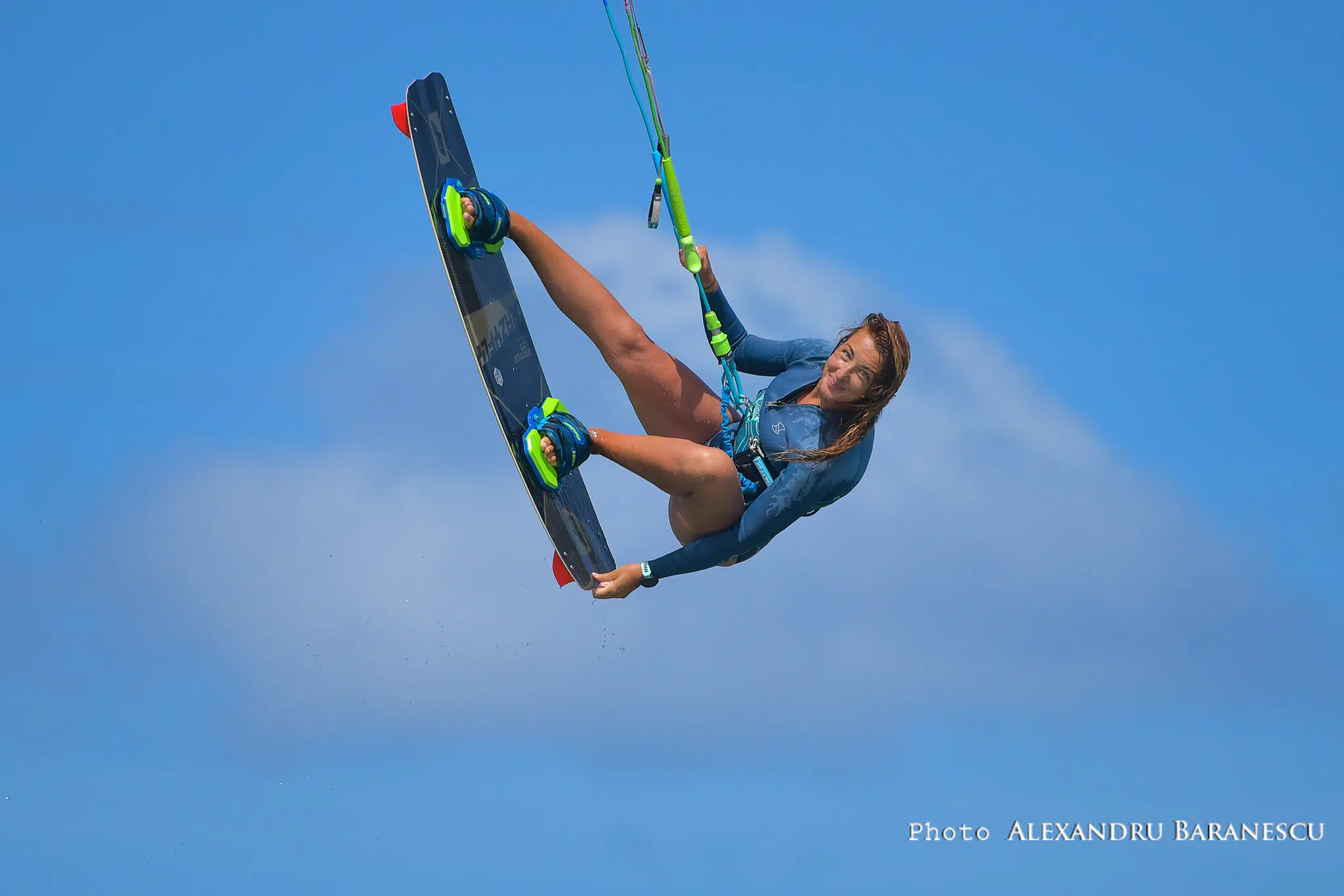 Kobieta w piance unosi się nad wodą na wyjeździe kitesurfingowym KiteAway, trzymając bar, na tle błękitnego nieba.