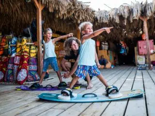 Dwóch chłopców ćwiczy na deskach pod okiem instruktorki w surf shacku - nauka przed wyjazdem na kite camp KiteAway w Egipcie.