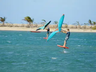 Dwie osoby na hydrofilach ze skrzydłami na wietrznej, niebieskiej wodzie przy plaży z palmami-idealne wyjazdy kitesurfingowe KiteAway.