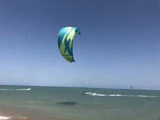 Kitesurfer na El Gounie z latawcem niebiesko-żółtym na tle błękitnego nieba; w tle drugi latawiec. Wyjazdy kitesurfingowe KiteAway.