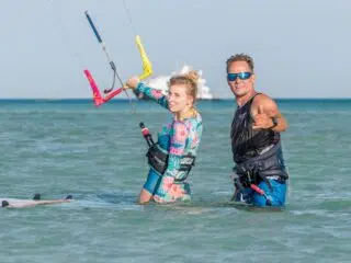 Uczestnicy KiteAway kite camp w piankach i uprzężach na płytkiej wodzie z barami do kitesurfingu, szkolenia, wakacje z kitesurfingiem.