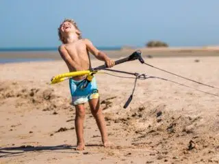 Chłopiec w kąpielówkach na plaży w El Gouna trzyma latawiec szkoleniowy. Wakacje z kitesurfingiem z KiteAway - kitesurfing Egipt.