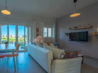 Nowoczesny salon z białymi sofami, idealny na relaks po wyjazdach kitesurfingowych KiteAway; widok zieleni i strefa jadalna.