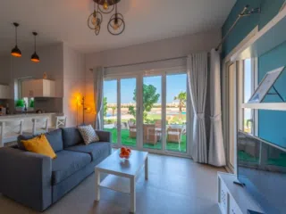 Jasny salon z szarą sofą, stołem i kuchnią, idealny na relaks po kite camp lub udane wakacje z kitesurfingiem z KiteAway.