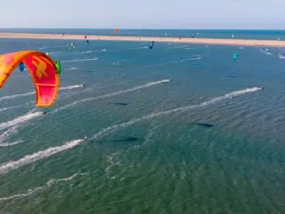 Lot z góry na kite spot KiteAway: liczne kitesurferzy na falach, kolorowe latawce i słoneczne niebo - idealne wyjazdy kitesurfingowe.